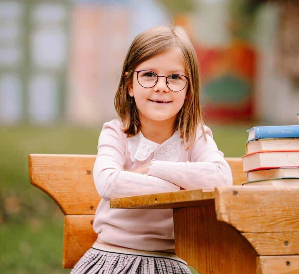 Mädchen mit Brille bei Schulfotografie im Freien, lachend und entspannt.