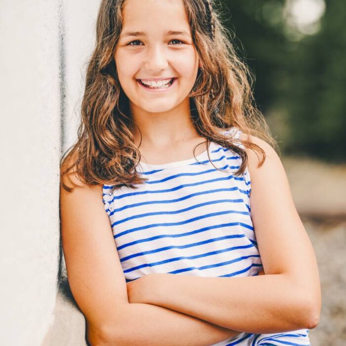 Fröhliches Mädchen bei Schulfotografie im Freien, lächelnd und entspannt.