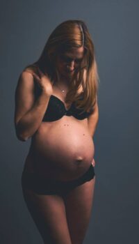 Schwangere Frau mit Babybauch in schwarzer Unterwäsche, emotionales Portrait.